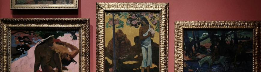 Tre dipinti post-impressionisti con cornici dorate appesi su una parete rossa in un museo